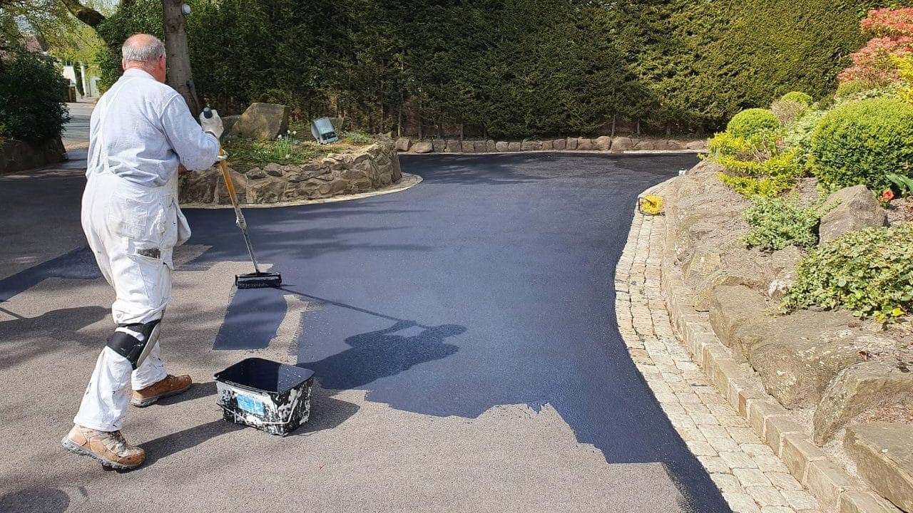 Technician in white overalls sealing a curved driveway by hand